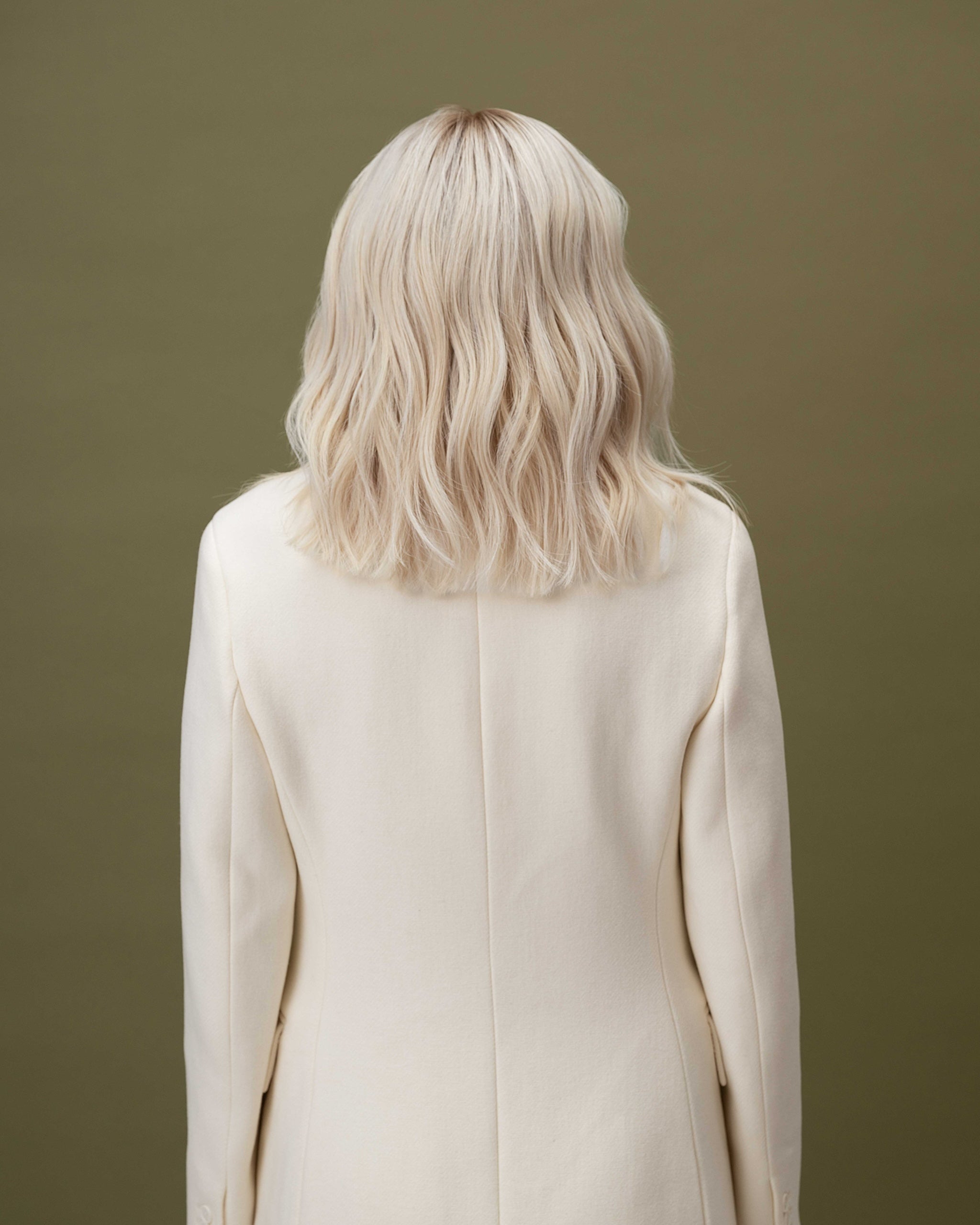 Fiorella Wig 35 cm human hair wig in platinum ash blonde with natural darker root, softly layered and shown from the back on model.