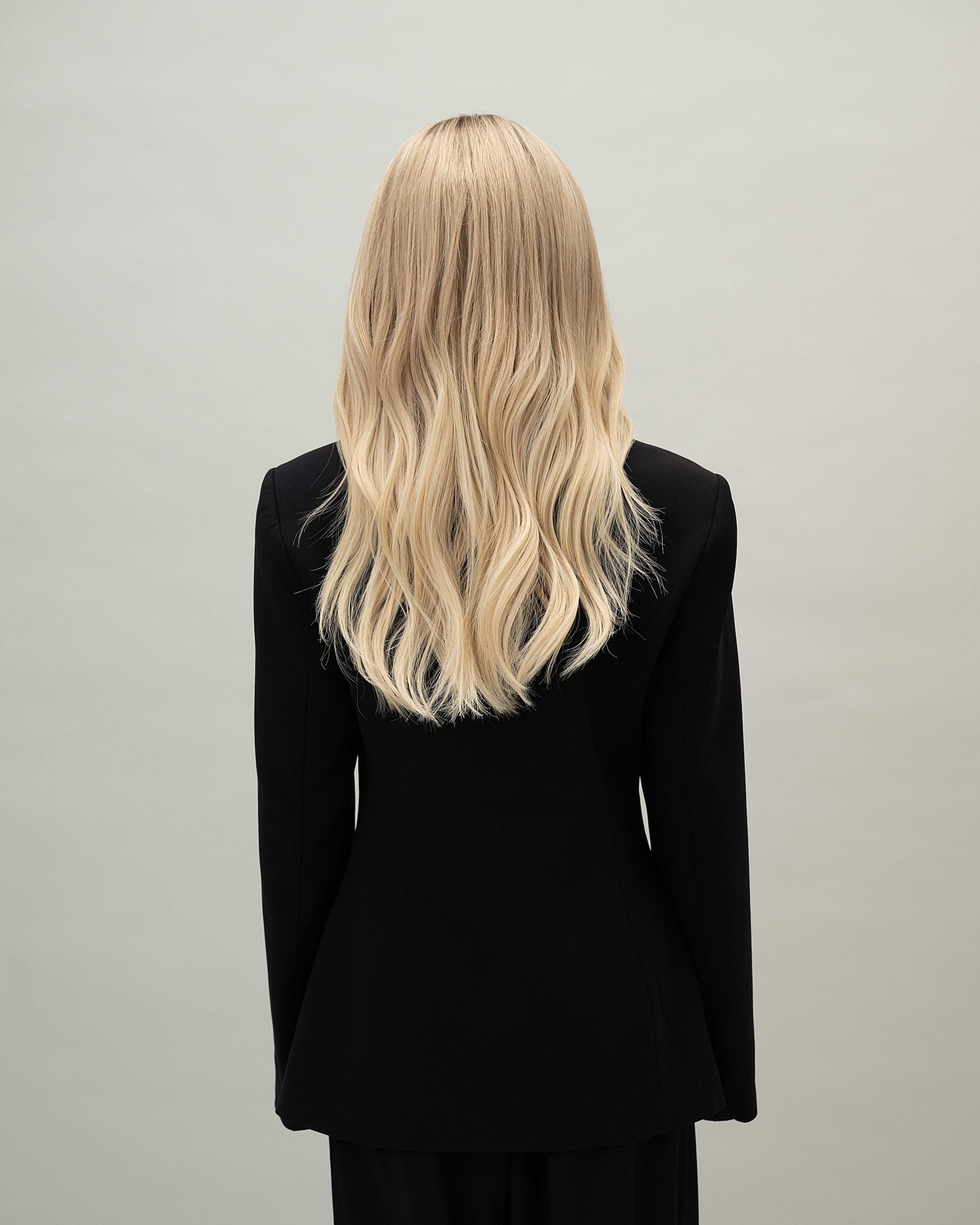 Vera Wig 40 cm light blonde human hair wig with natural darker roots, softly layered cut for volume and movement, shown from the back on model.