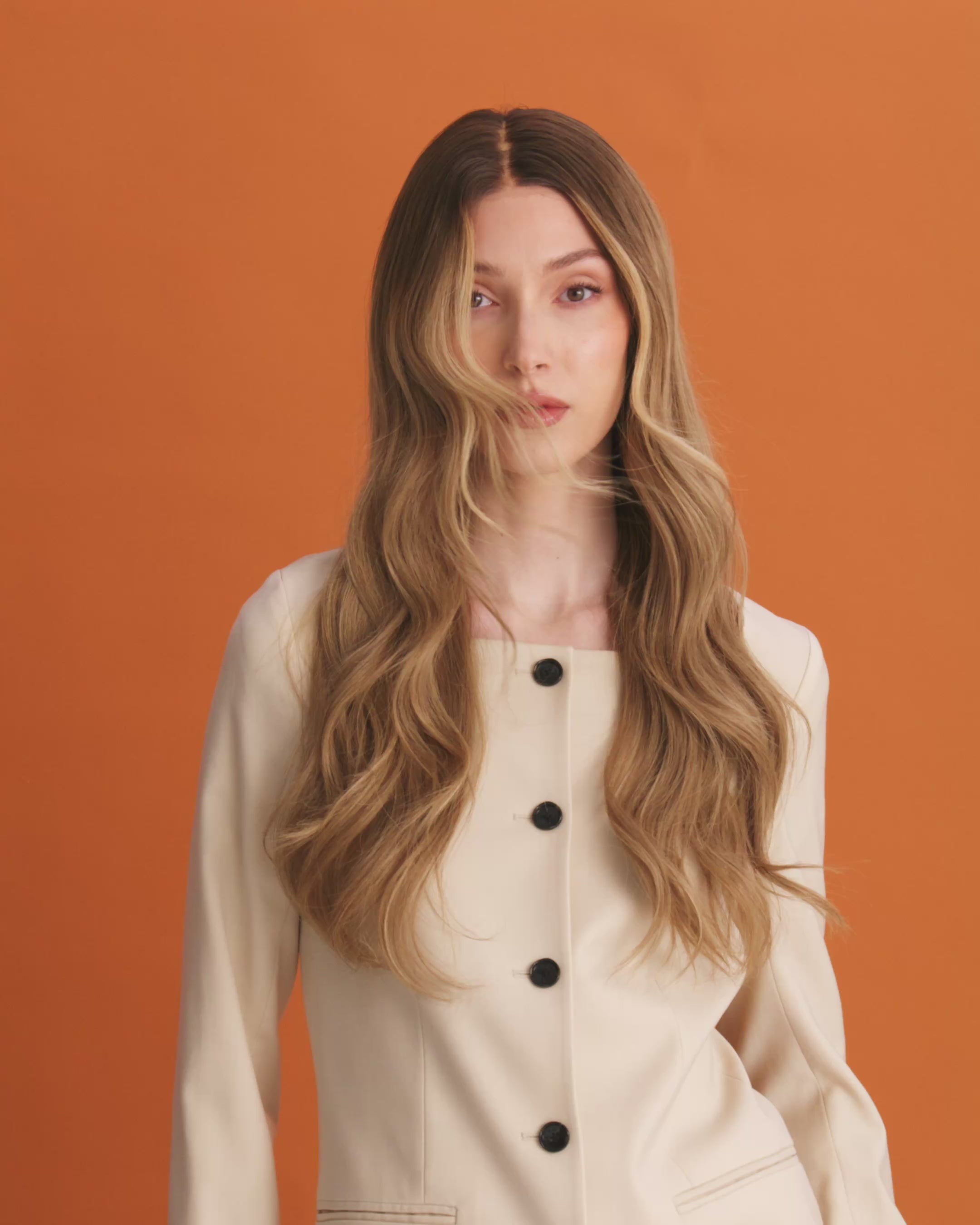 Noble Nightshade Wig 50 cm softly layered with dark blonde roots and beige blonde tones, featuring money-piece highlights around the face, shown on model, in the video you can see how the hair has a natural movement.